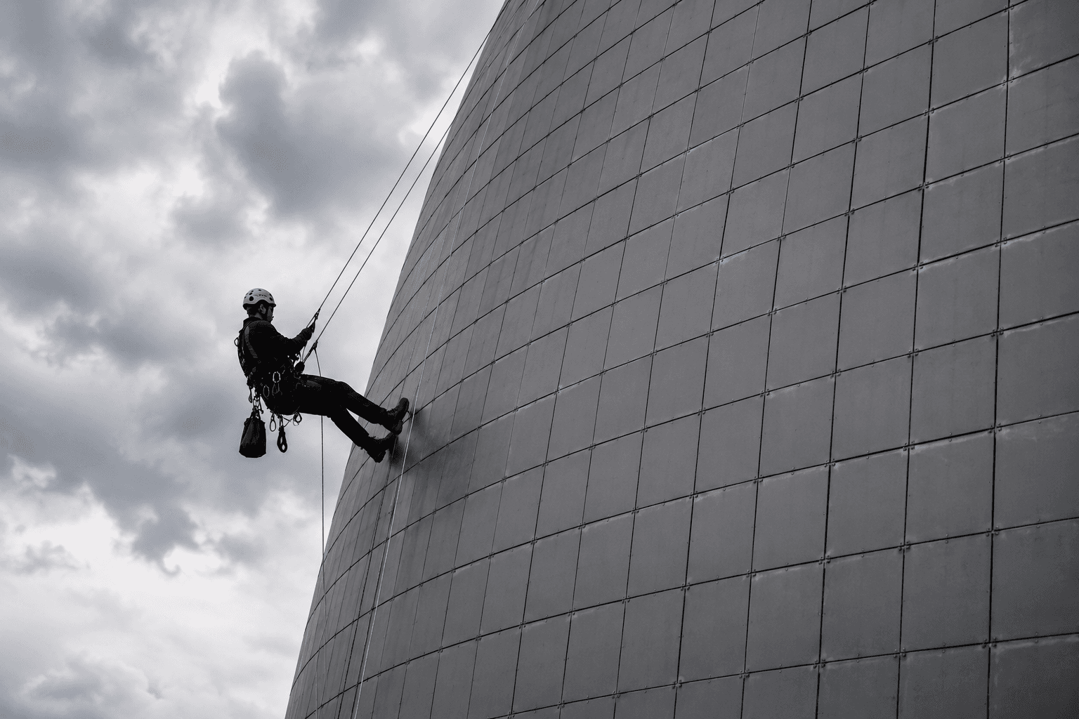 Silhouette d'un cordiste sur une façade courbe en métal d'une tour contemporaine